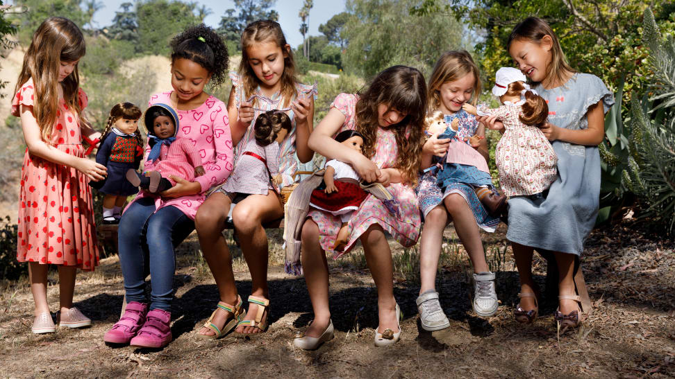 A group of six girls sitting on a bench each holding a different American Girl doll