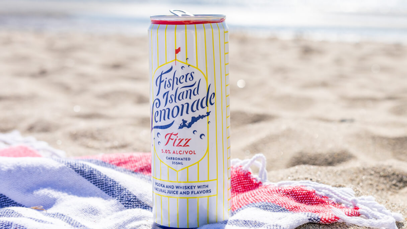 A can of spiked lemonade sits atop a beach towel on a sandy beach.