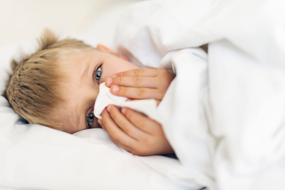 Little boy looking distraught while blowing his nose.