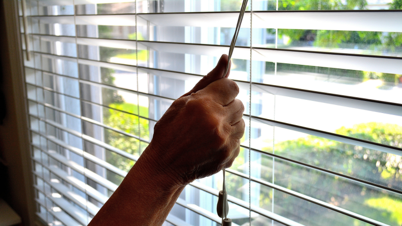 a person holds onto a cord and closes window blinds in front of a window during the day