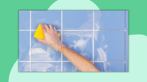 A hand wearing a glove washes a tiled wall with a sponge.