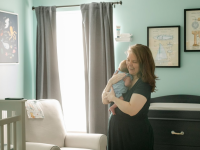 Person smiling while holding newborn baby in arms inside of nursery room.