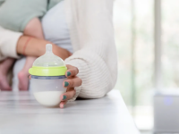 A parent reaches for a baby bottle filled with baby formula or breast milk while she holds her infant.