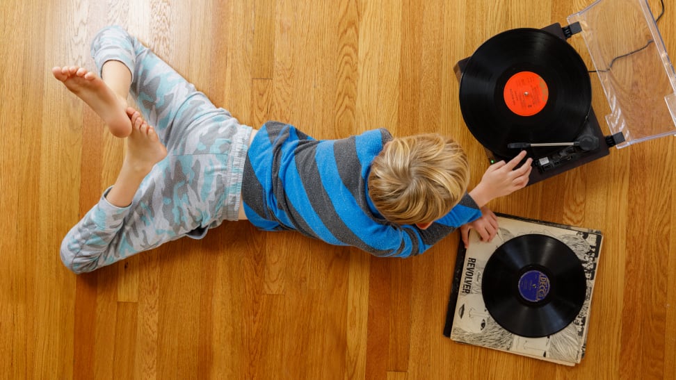 A child laying on his stomach on the floor listening to a record player.