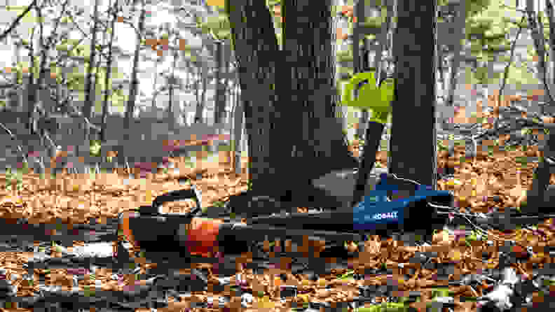 Three leaf blowers are on display leaning up a tree and laying on the forest floor.