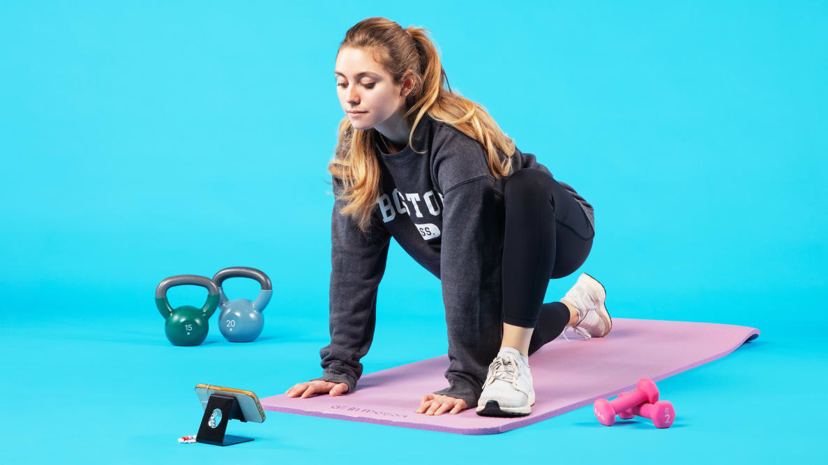 Person stretching on pink yoga mat with the FitOn app next to kettlebells and small weights.