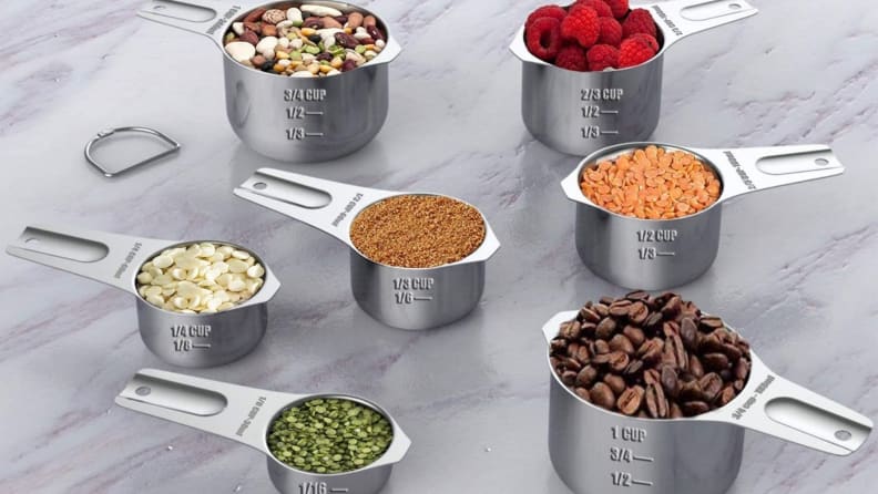 A set of stainless-steel measuring cups contains various seeds, berries, coffee beans, and so forth.
