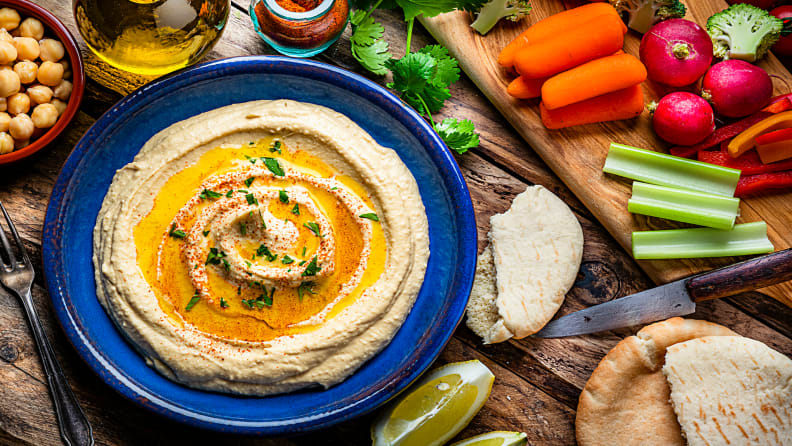 Vista superior de un plato azul de hummus y aceite de oliva sobre una mesa rústica de madera con pan de pita y un entorno áspero