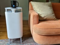 A standing air purifier placed in a living room next to a sofa.