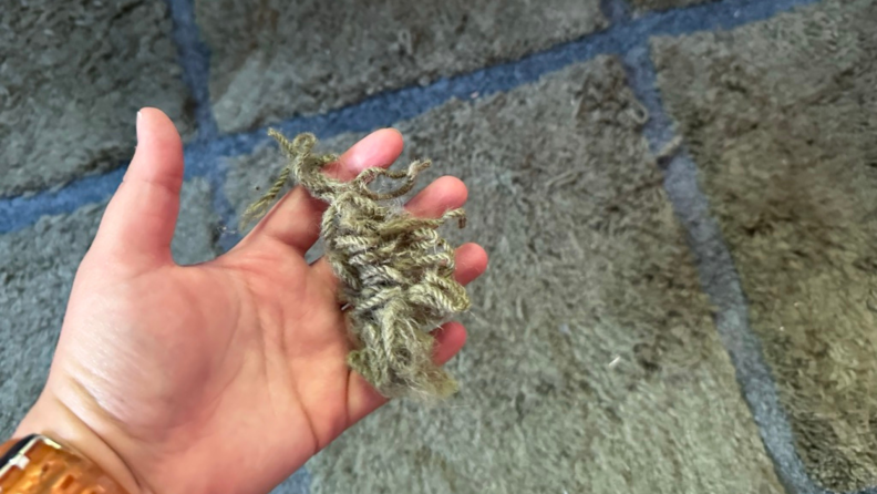 A hand holding a bundle of yarn that’s been pulled off the rug.
