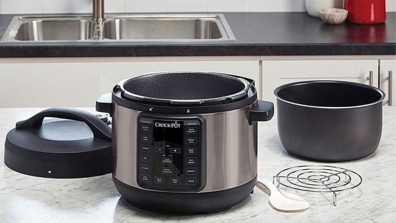The Crock-Pot Express Easy Release 6-Quart multi cooker is on a kitchen counter, alongside its accessories such as lid, steamer, and the inner pot.