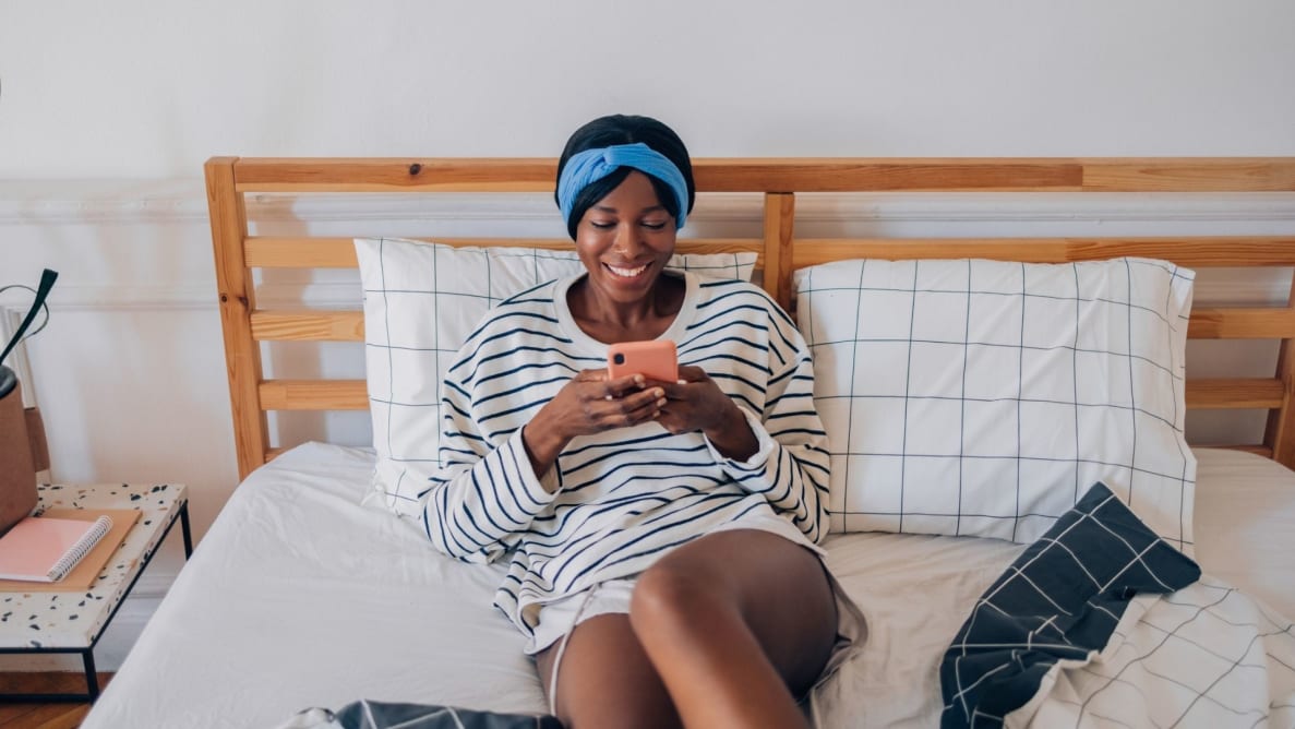 Person looking at phone and sitting up in bed made with sheets