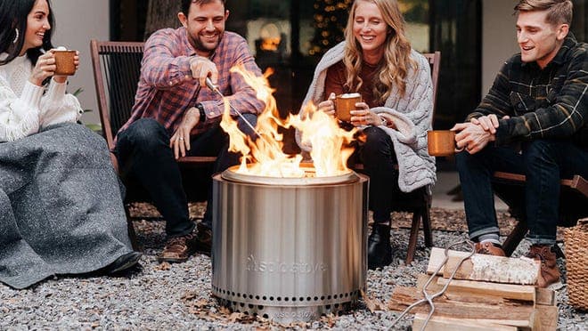 Four people drink cocoa and roast marshmallows outside.