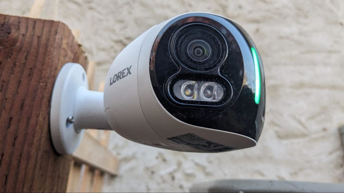 The Lorex 4K Dual-Lens Wi-Fi Security Camera hangs on an outdoor fence post.