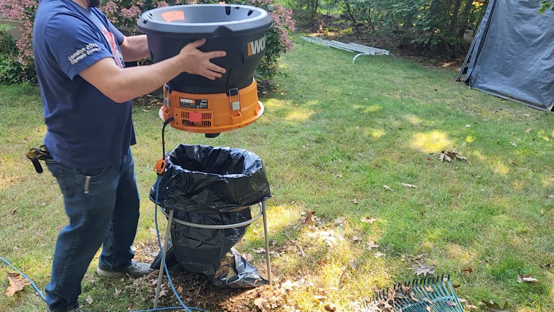 A person outdoors putting the Worx Electric Leaf Mulcher onto its stand, which is fitted with a large black garbage bag.