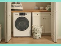 A GE washer-dryer combo is nestled in a small laundry closet with a basket of clothes beside it.