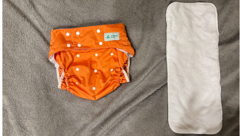 Orange diaper next to a diaper insert on a gray fabric.