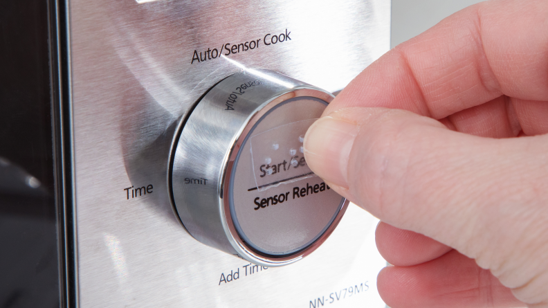 A hand places a braille label on the start function of an oven