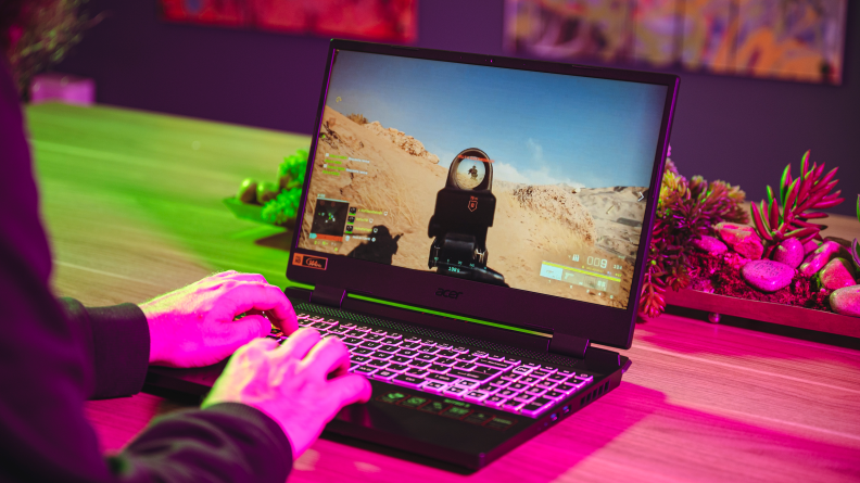 An open and powered on laptop with a pair of hands over the keys playing a game