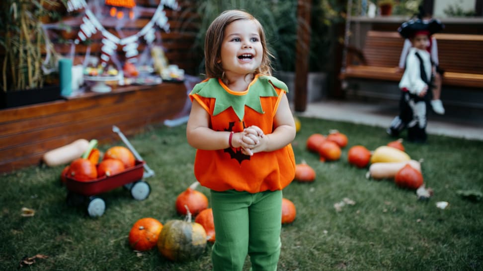 Child smiling outdoors while dressed in jack-o'-lantern Halloween costume.