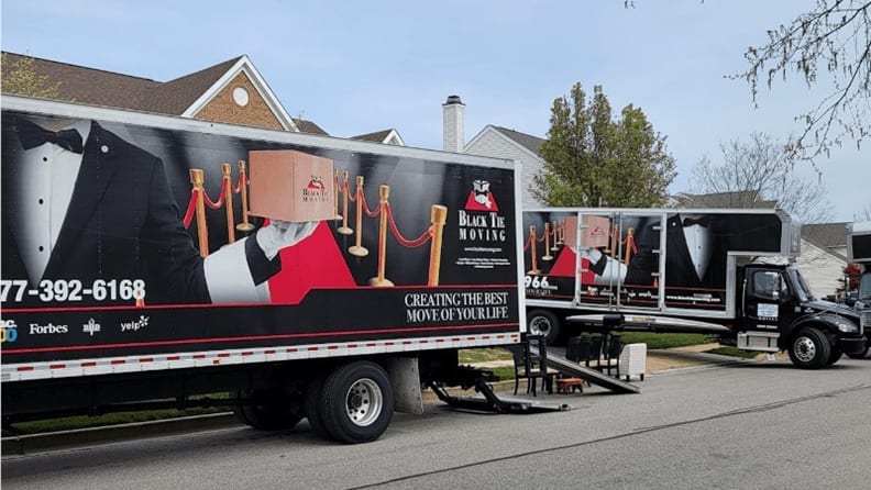 Two moving trucks parked on the street with ramps attached to one truck
