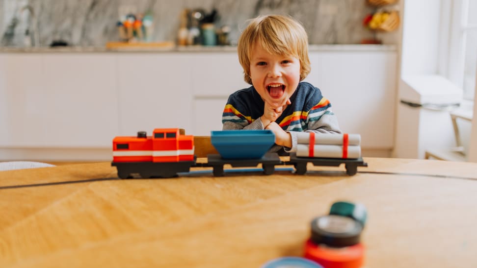 A boy laughing standing next to a toy train