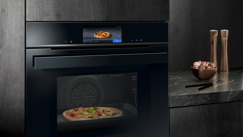 A black BoschSiemens AI iQ700 Oven cooking a pizza in a darkly colored kitchen.