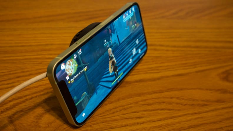 Una toma en ángulo de un iPhone 12 Mini, con el ventilador conectado, apoyado por el Phone Cooler, con Genshin Impact en la pantalla.