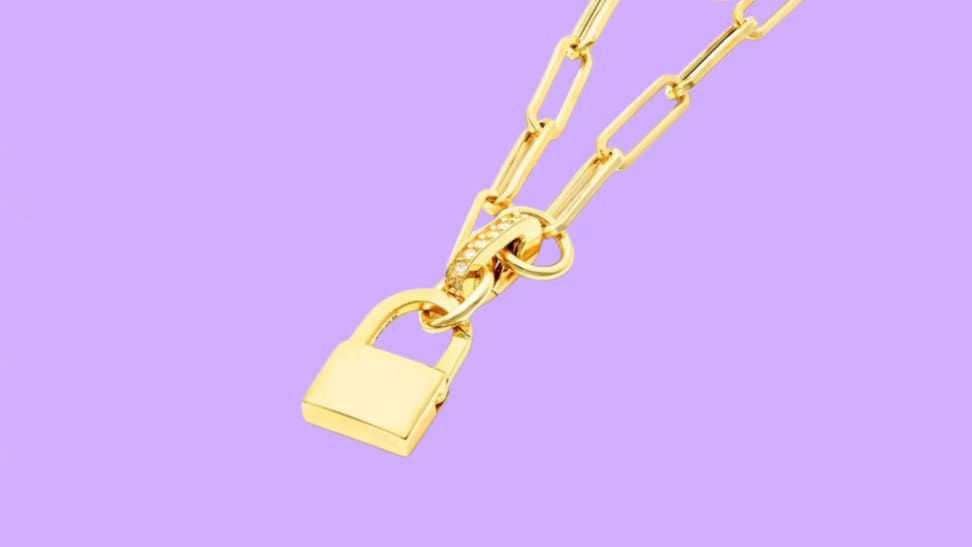 An image of a gold padlock charm on a gold paperclip chain necklace.