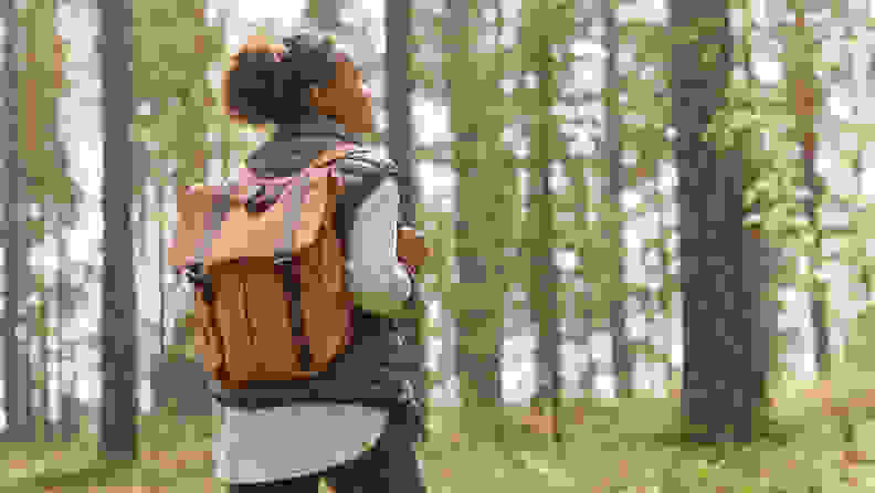 A woman hiking in the woods with an orange backpack.