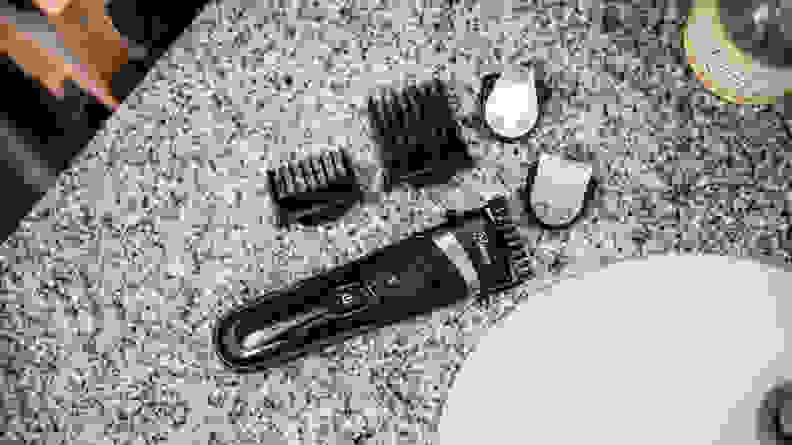 A Hatteker Hair and Beard Trimmer and its accessories sit on a marble countertop.