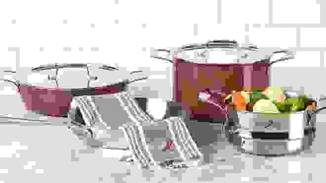 灶台上放着银色和红色的锅碗瓢盆，其中一个里面放着蔬菜。