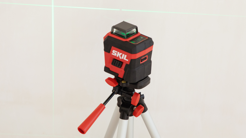 A red laser level on a tripod shoots a green laser onto a wall.