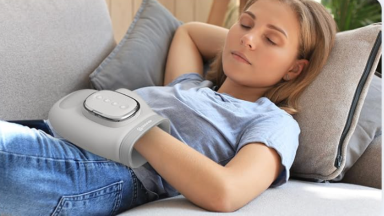 A woman lays on a couch with her hand in a hand massager