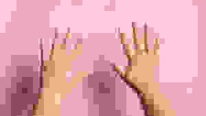 Two hands with press-on nails on them held up in front of a pink wall.