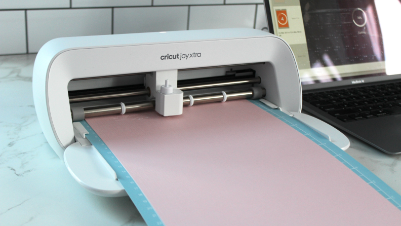 The Cricut Joy Xtra cutting an intricate design on a piece of pink cardstock.