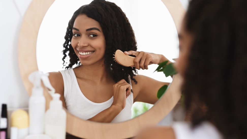 A woman sitting at a vanity brushing product through her hair