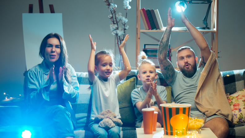 Family smiling and enjoying movie in front of projector screen.