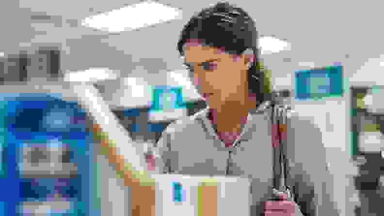 Woman reading over-the-counter teeth whitening product label at pharmacy