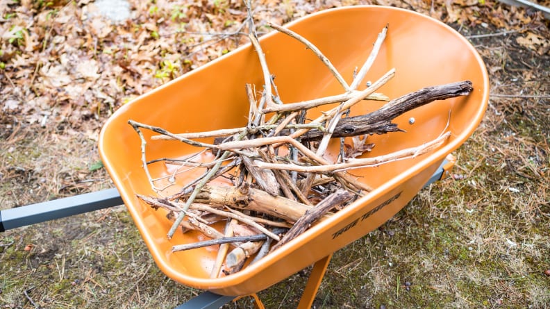 An orange wheelbarrow holds a bundle of branches and sticks.