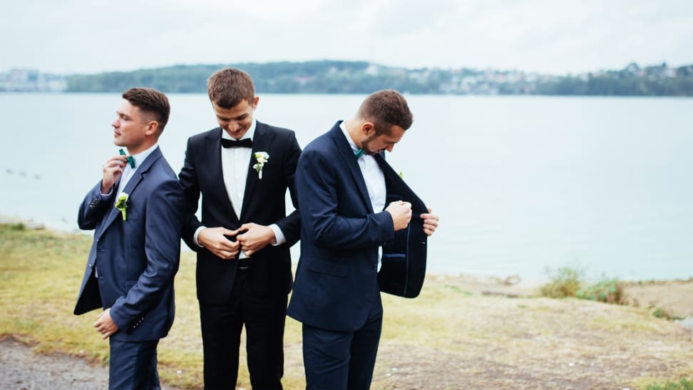 Three men standing outdoors wearing different types of suits and tuxedos.