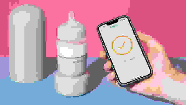A person holding a smart phone next to the Ember Baby Bottle System on a blue and pink background.