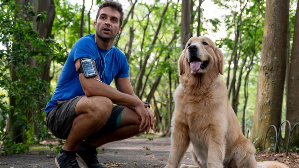 A runner bends down next to their dog on a wooded running path