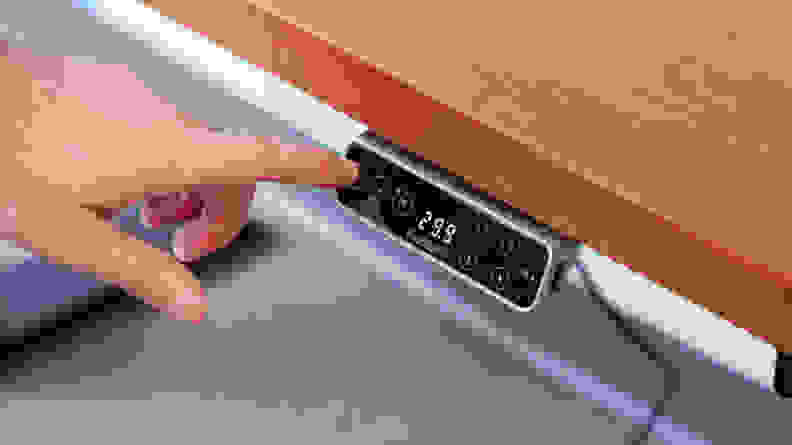 A finger pressing the button to lower the standing desk's height.