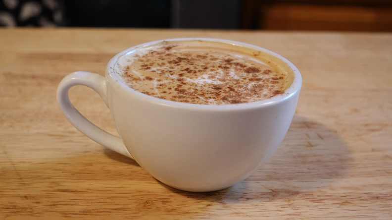 A hot pumpkin spice latte in a white mug on a wooden counter.