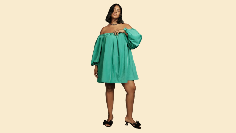 A model wearing a green knee-length dress with off-the-shoulder sleeves.