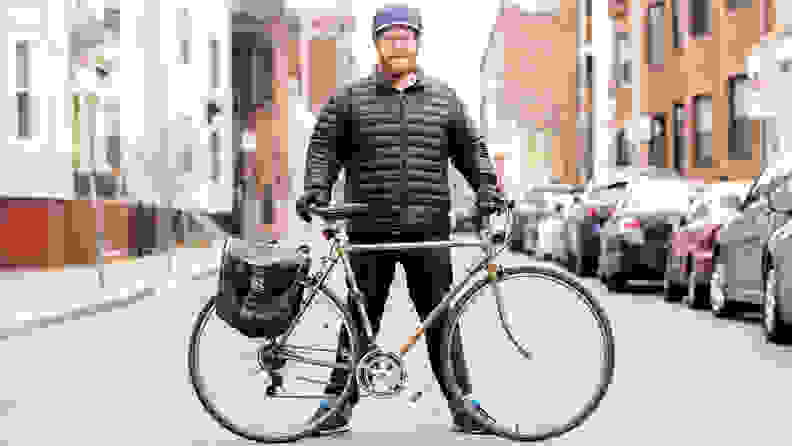 A man standing behind his bicycle in the road.