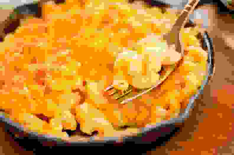 A cast iron pan full of macaroni and cheese is in the center of the image.