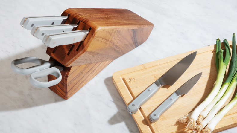 The Misen knife block sits on the counter with 3 knives and a sheer in it, and 2 knives sit next to scallions on a cutting board.