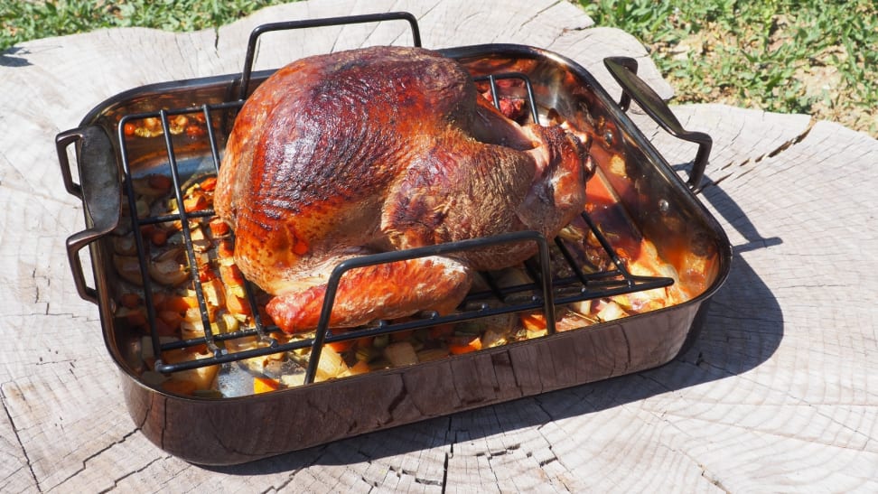 A smoked turkey perched in a roasting pan lines with veggies and aromatics.